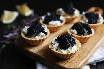 Board of delicious tartlets with black caviar and cream cheese on wooden table, closeup