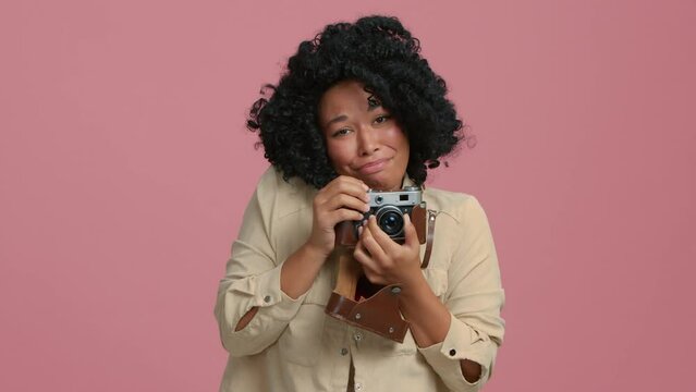 Slow Motion young creative photographer woman of color taking a cute adorable photo with vintage film camera. Positive touched African American girl 20s smiling after making shot on retro photo camera