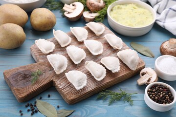 Raw dumplings (varenyky) and ingredients on light blue table