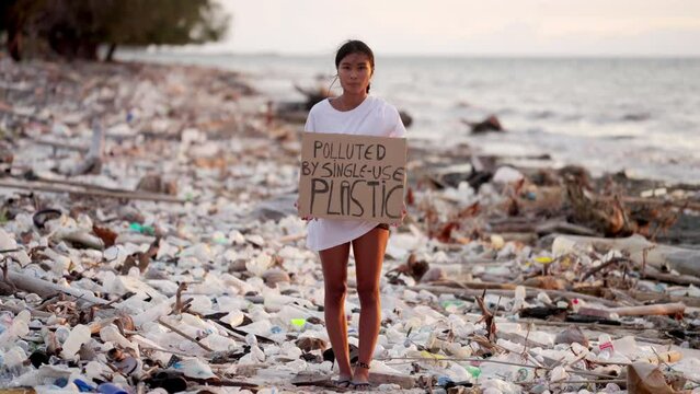 A woman holding sign to stop using single use plastic bottles. The beach covered with plastic trash. Ocean pollution