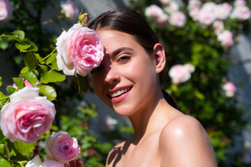 Naklejka premium Woman enjoying a day in the park on summer. Lifestyle and wellness. Beautiful natural woman in the garden of roses. Sexy woman enjoying flowers over spring garden background. Rose spring garden.