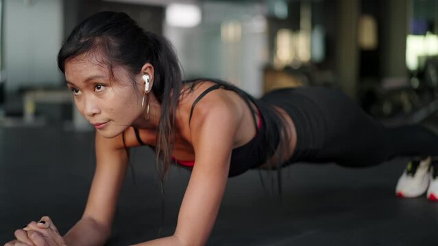 Attractive young asian woman doing elbow plank holds at the gym. Fit girl training at fitness center