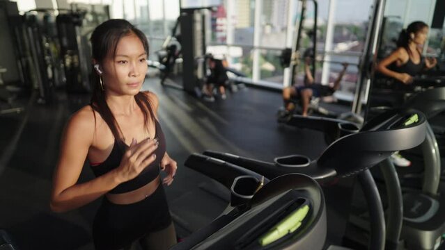 A young asian woman runs on treadmill in gym. Athletic girl running workout for weight loss