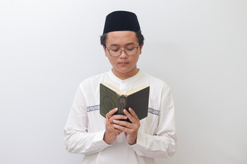 Portrait of young Asian muslim man reading and reciting Holy book of Quran seriously. Isolated image on white background