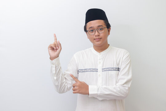 Portrait of young Asian muslim man showing product and pointing with his hand and finger. Isolated image on white background