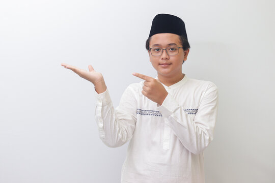 Portrait of young Asian muslim man showing product and pointing with his hand and finger. Isolated image on white background