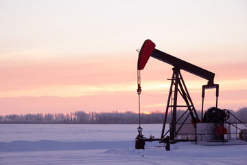 Pink sunset in the oil field with pump jack in winter.