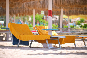 Straw shade umbrellas on sea tropical beach with resting sunbeds against blue vibrant sky in summer