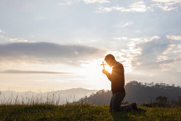 Male Travel holding christian cross praying alone on top mountain sunset background Lifestyle...