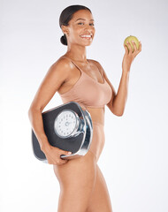 Portrait, black woman and body with apple, scale and diet for weight loss, health and wellness on grey studio background. Face, African American female and happy lady with fruit, fitness or nutrition