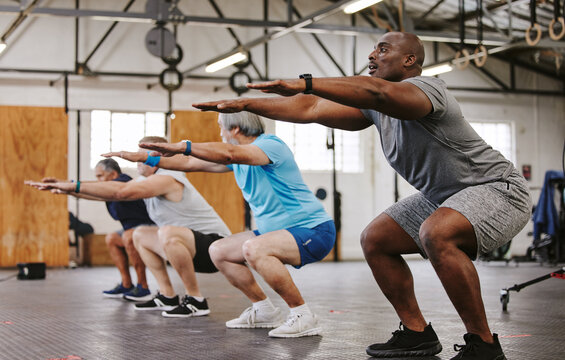 People, fitness and stretching in class at gym for workout, squat exercise or training together. Diverse group or team in warm up stretch session for sports, health and cardio wellness at gymnasium