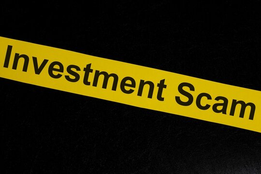 Investment scam and fraud alert, caution and warning concept. Yellow barricade tape with word in dark black background.