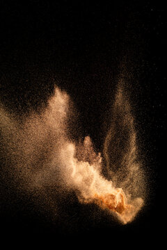 Brown color sand splash against black background. Sand fly wave in the air.