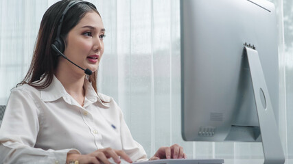 Asian customer support operator wearing headset and microphone working at her desk with laptop....