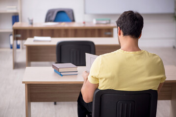 Young male student teacher sitting in the classroom