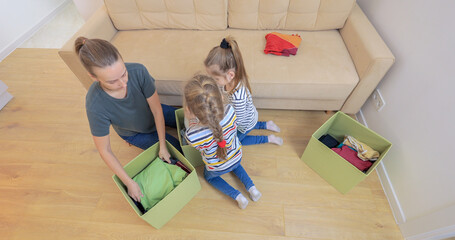 Young woman and her daughters puts clothes in boxes. Donation.