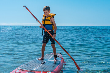 A 9-year-old white boy from Eastern Europe learns to paddleboard in the sea. Front view