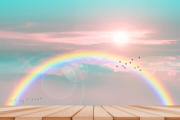wood top table and sunrise and rainbow on sky with pastel blue tone cloud and fog over on the top mountain with birds flying