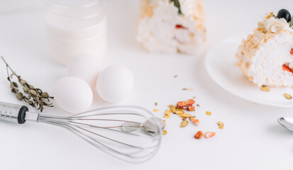 Meringue roll without sugar on white plate cut into pieces in front of bottle of milk and eggs.