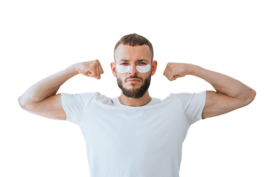 Serious beardy Italian young man in white t-shirt with white skin care patches applied  on skin below eyes bends hands shows biceps looks at camera over transparent background. Cosmetology, healthcare