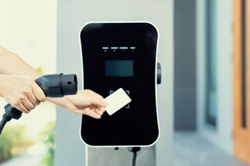 Hand holding credit card to pay public charging station and recharge her electric vehicle,...