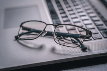 Glasses and a laptop on a black table, backlight. Close-up