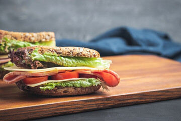 Sandwich with a ham, cheese, tomato, salad lettuce on a wooden board. Lunch concept with copy-space