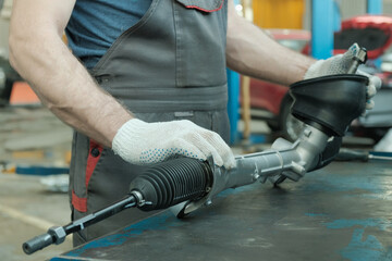 In the hands of an auto mechanic, a steering rack for a passenger car. A car service specialist...