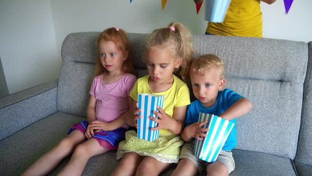 Mother hand give popcorn boxes for children watching tv television. Little kids eating pop corns and watching home cinema. Smooth camera motion shot with gimbal.