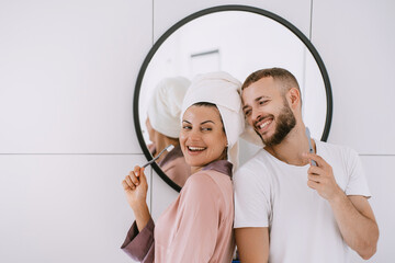 Cheerful caucasian young couple at bathroom brushing teeth toothy smiling cuddling. Newlyweds...