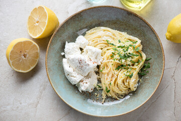 Plate with spaghetti, ricotta cheese and lemon zest, elevated view on a beige stone background, horizontal shot