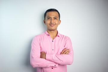 Portrait of confident smiling Asian young man wearing pink shirt standing with arms folded isolated on white background.