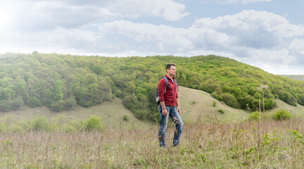 Adult man with backpack climbs the green hills and admires the s
