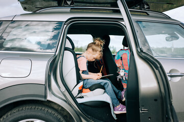 young girl sat drawing in the car on a road trip
