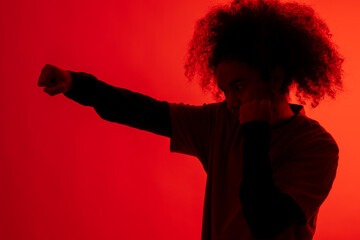 Silhouette with red light of boxer attacking. Young man with afro hair on white background