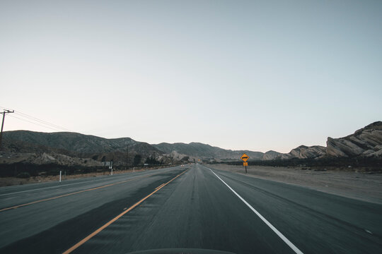 Empty Highway in California Right after Sunset with Yellow Road Sign and Mountains in the distance during Coronavirus Pandemic