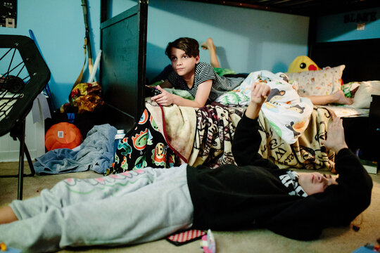 Boy on his bottom bunk bed playing video games and sister on the floor