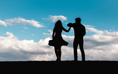 Silhouette of man and woman dancing against a blue sky with clouds.