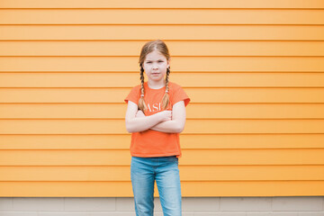 Young girl standing with crossed arms in front of orange wall