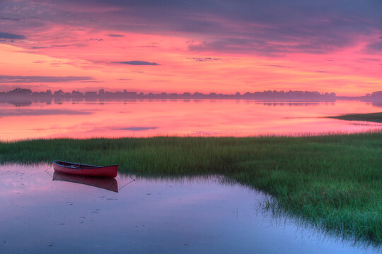 Red canoe floats in Maine tidal marsh amidst dramatic dawn light.