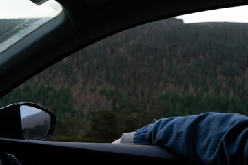 A passenger wearing a denim jacket leans their arm out the window
