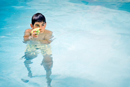 Handsome, dark-haired boy playing with a water gun in the pool water