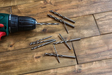 On the wooden surface is a drill and scattered drills of different diameters