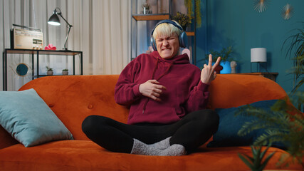 Happy rocker woman with short hair in wireless headphones relaxing at home dancing on couch...