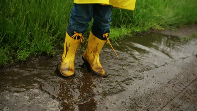 Young child jumping and splashing in mud puddle in road
