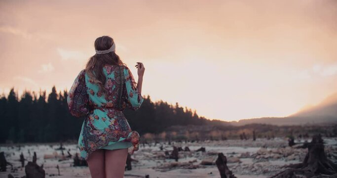 Fashion shot of a girl dressed in boho floral dress walking in shallow water at sunset, Panning in Slow Motion