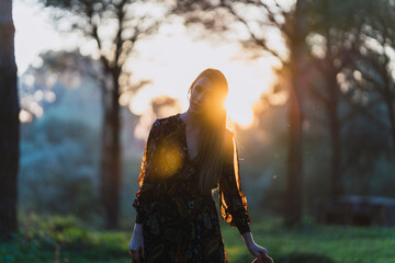 Chica joven delgada de pelo largo con sombrero y ropa otoñal posando al atardecer en un bosque