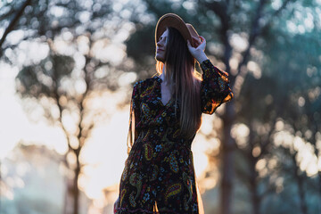 Fototapeta na wymiar Chica joven delgada de pelo largo con sombrero y ropa otoñal posando al atardecer en un bosque