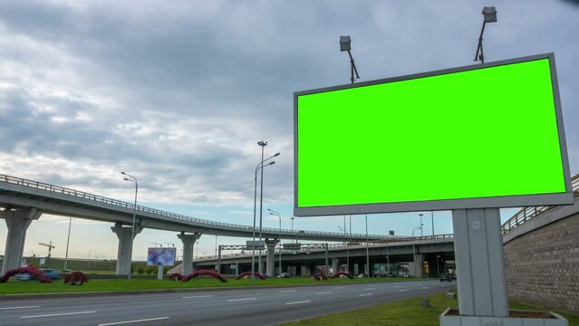 Time lapse shot of vehicles moving on road by green blank billboard against cloudy sky