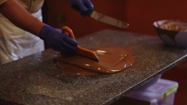A man in apron skillfully stirs milk chocolate on a marble tabble